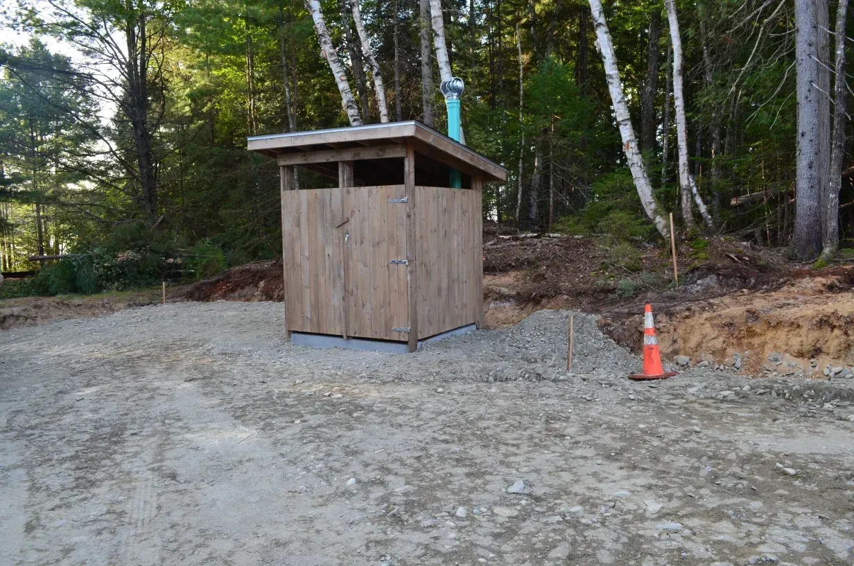 A wooden shed is sitting in the middle of a dirt field in the woods.