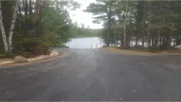 A road leading to a lake surrounded by trees on a cloudy day.