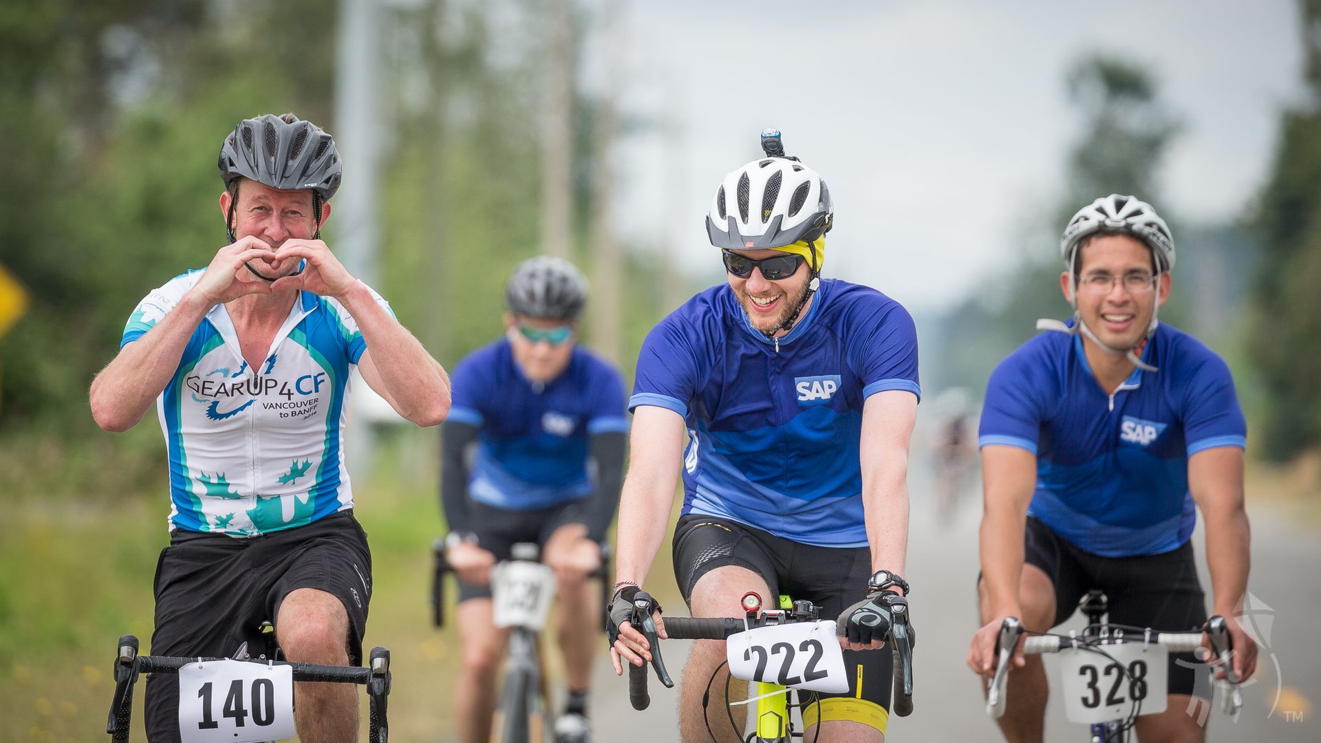 Four riders on their bike. One making a heart ship with their hands.