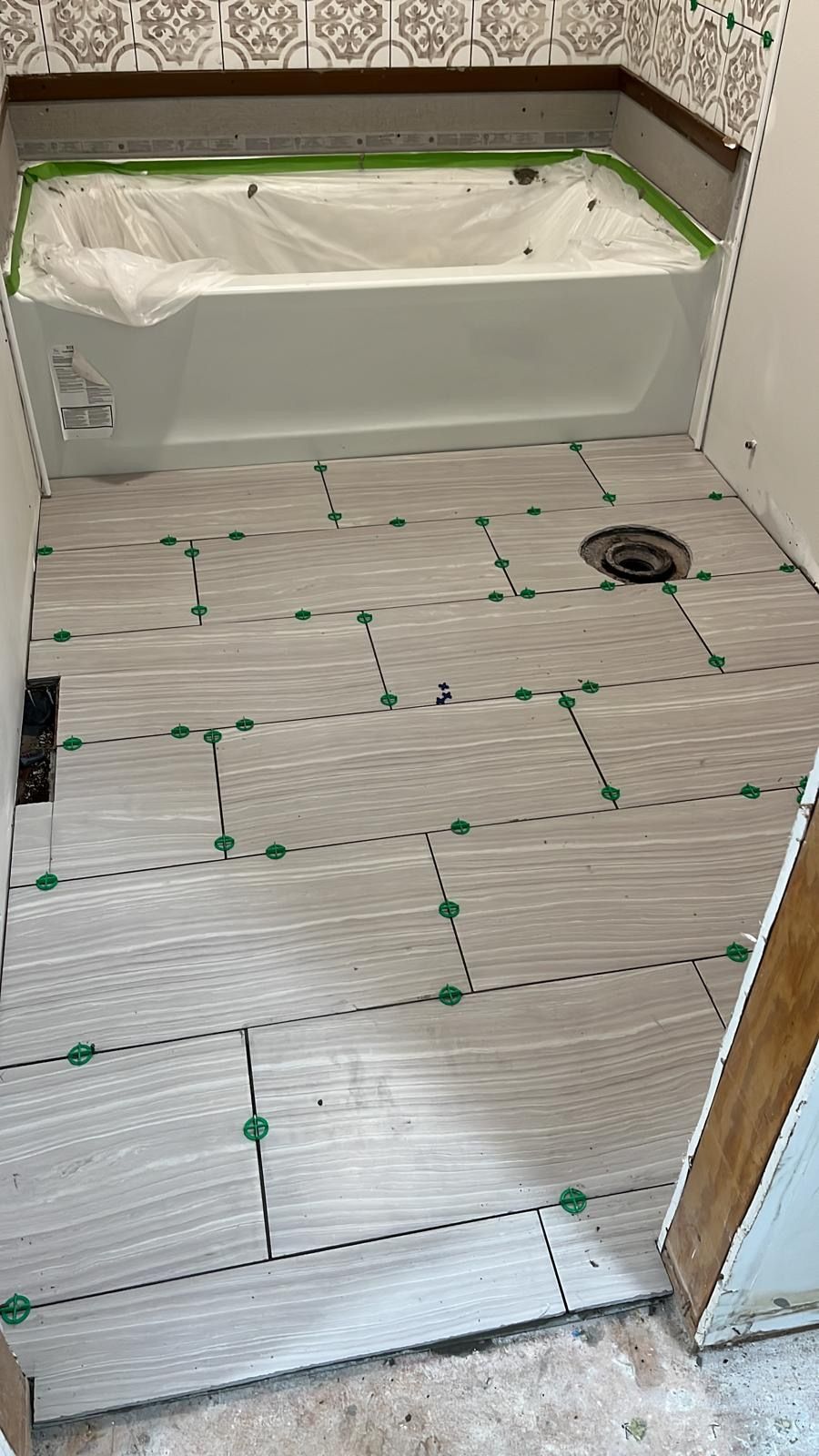 Partially tiled bathroom floor with green spacers and a bathtub under renovation
