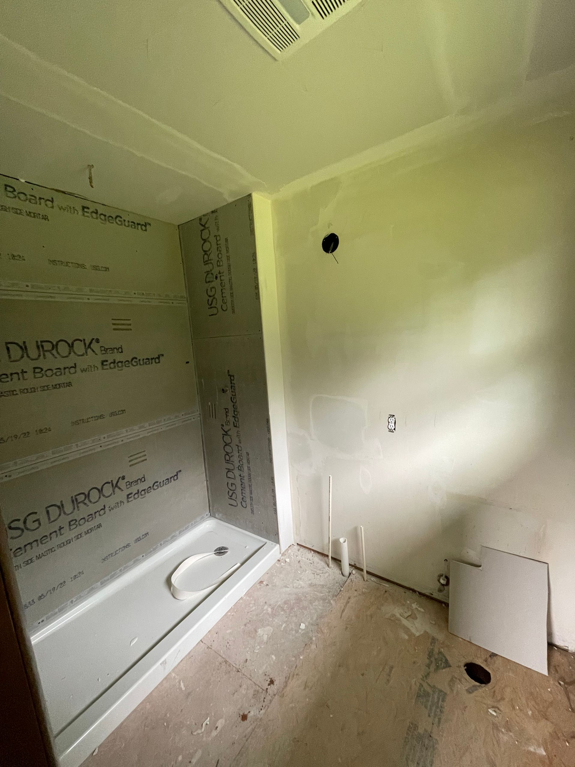 Partially tiled bathroom under construction with bathtub, wall openings, and debris on the floor