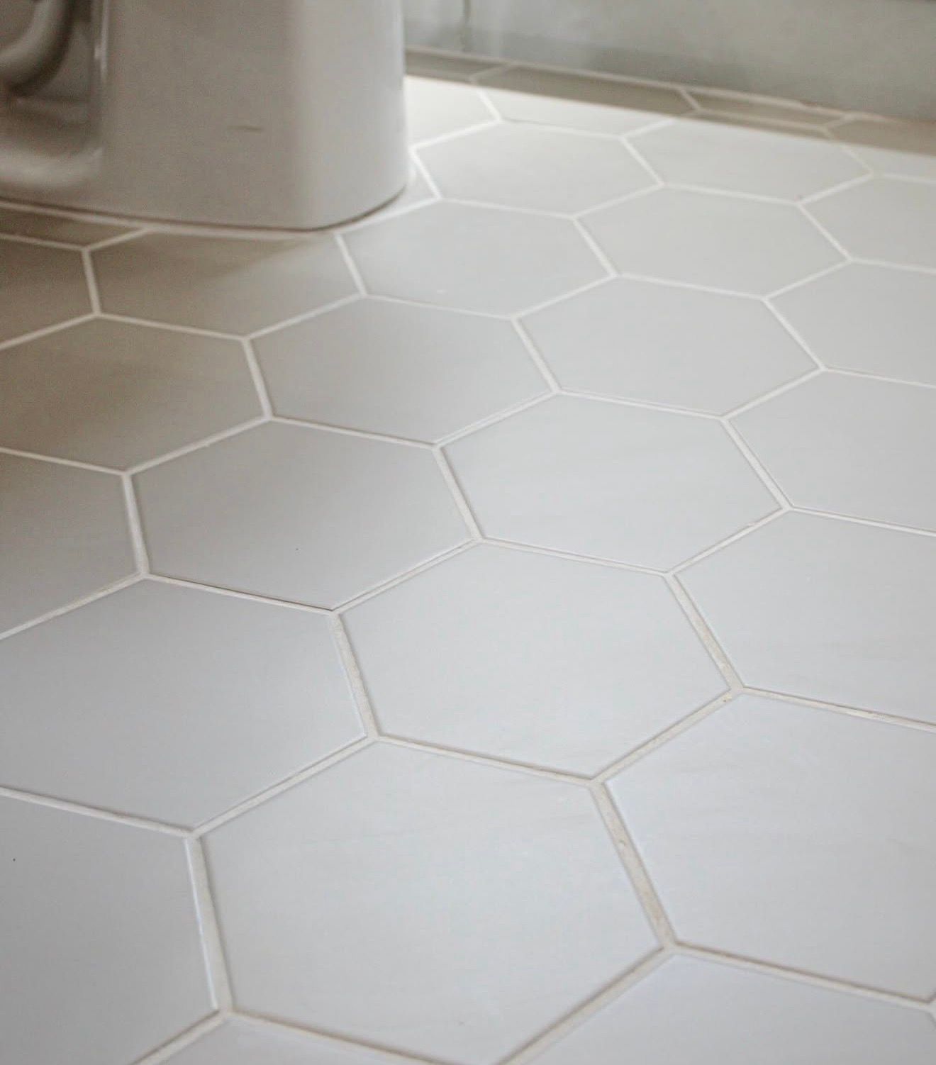 White hexagonal tiled floor with light grout lines beside a gray object