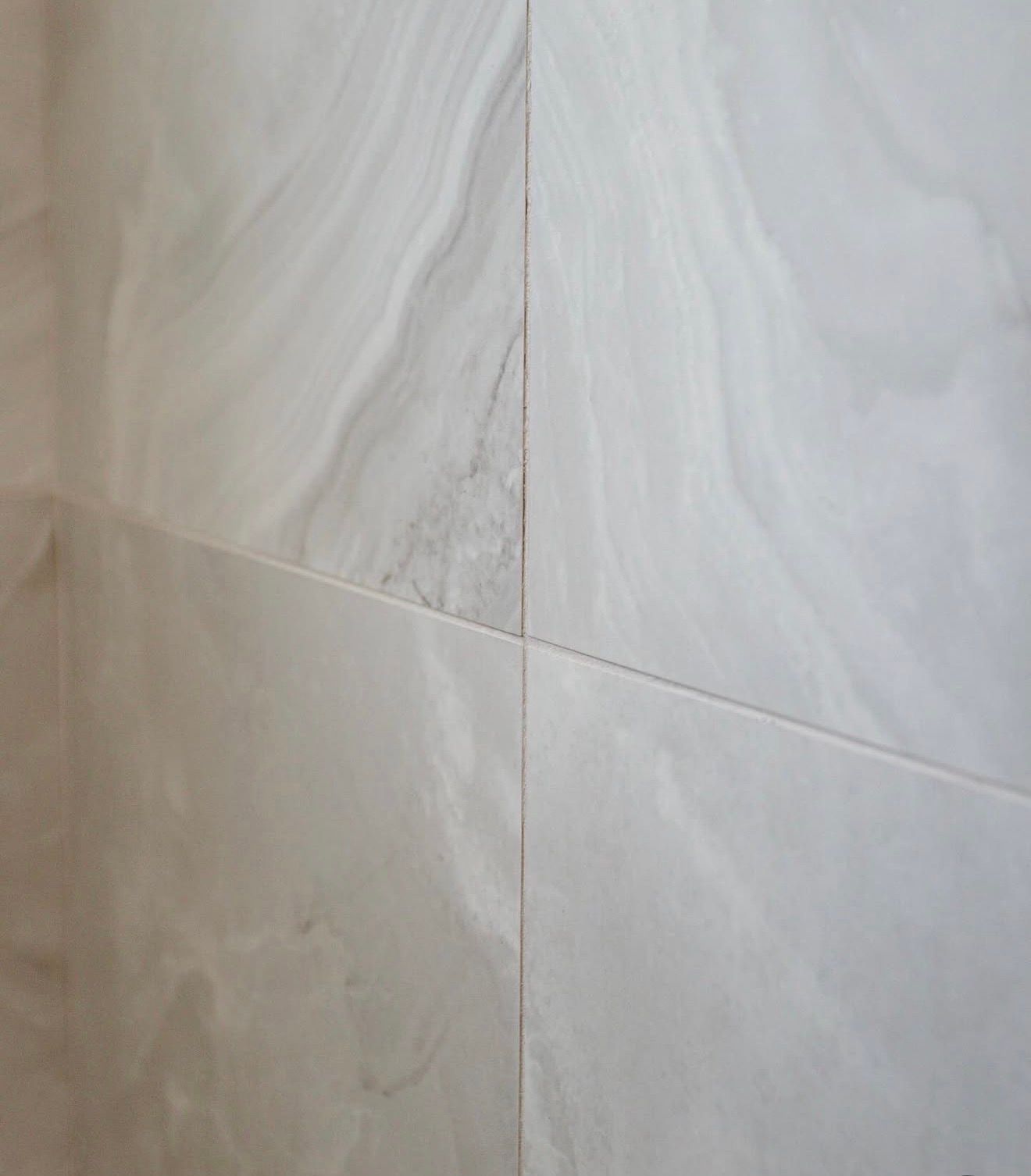 Close-up of pale marble tile wall with diagonal grout lines and subtle veining