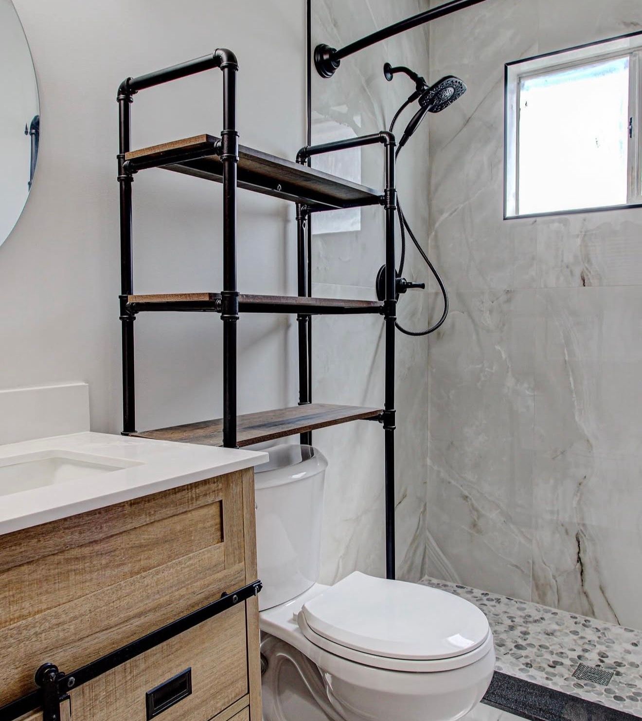 Modern bathroom with toilet, shower, black shelf unit, wood vanity, and marble-look walls and floor