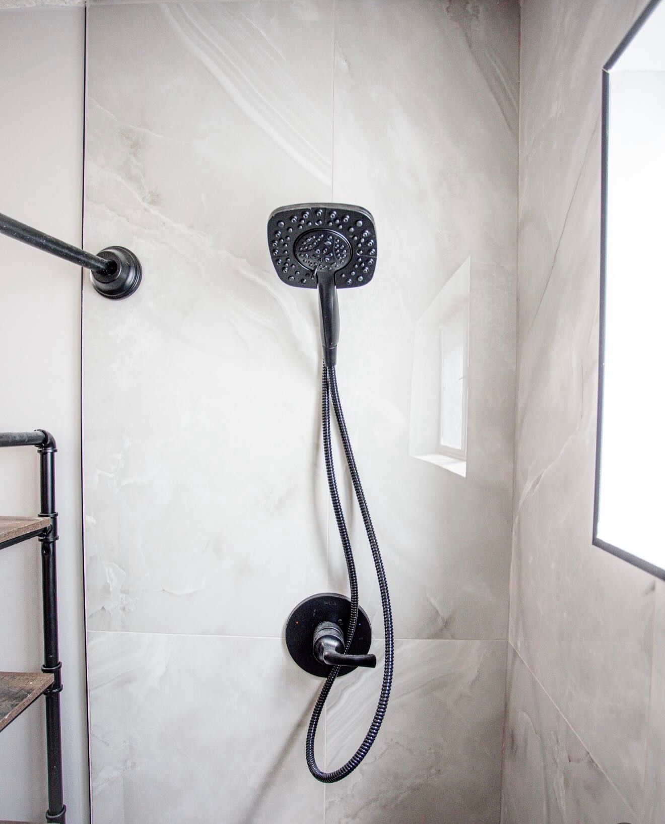 Black shower fixture with rainhead and handheld sprayer in a light tiled shower stall