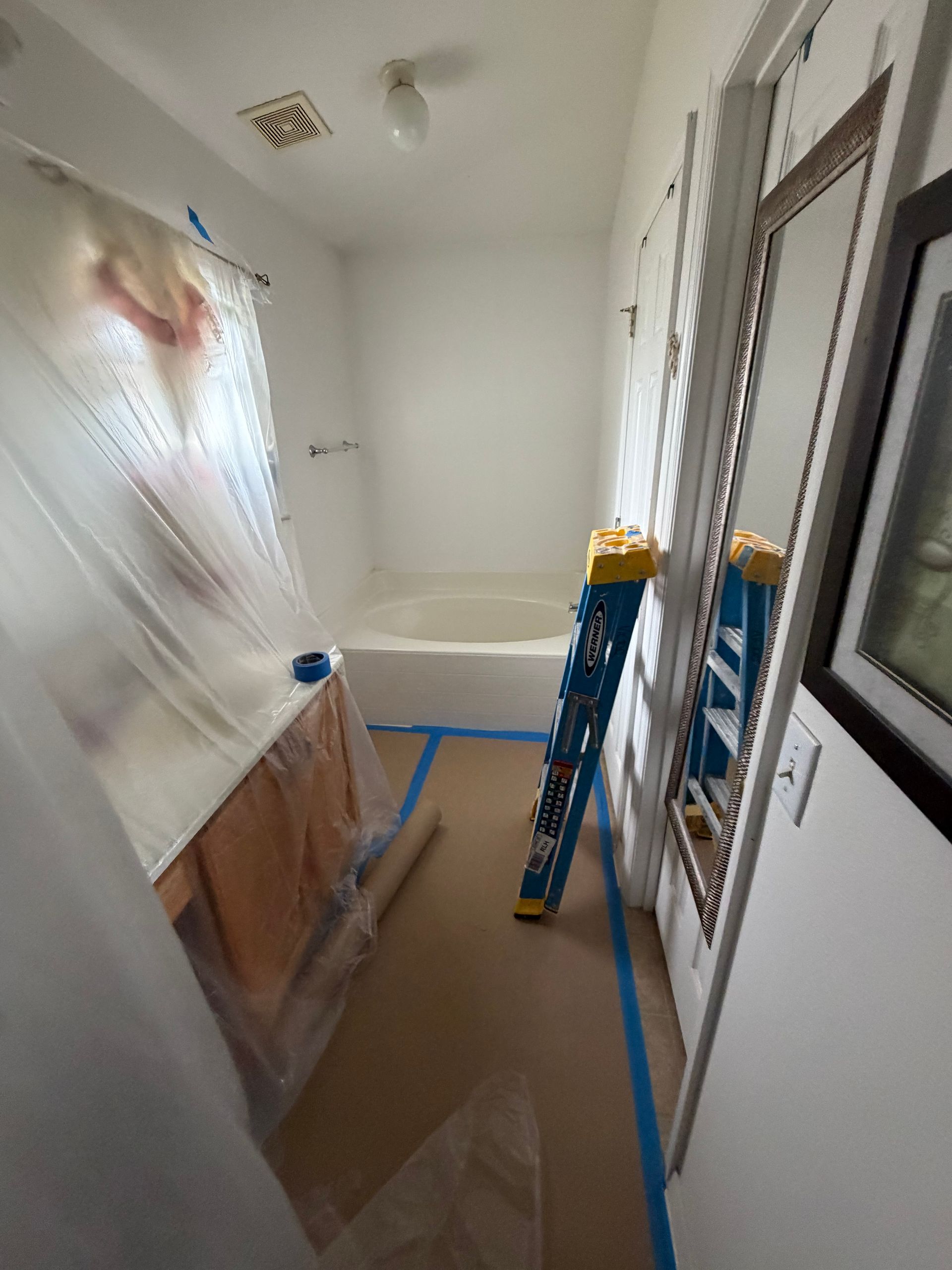 Renovation room with plastic-covered furniture, ladder, and blue painter’s tape on the floor