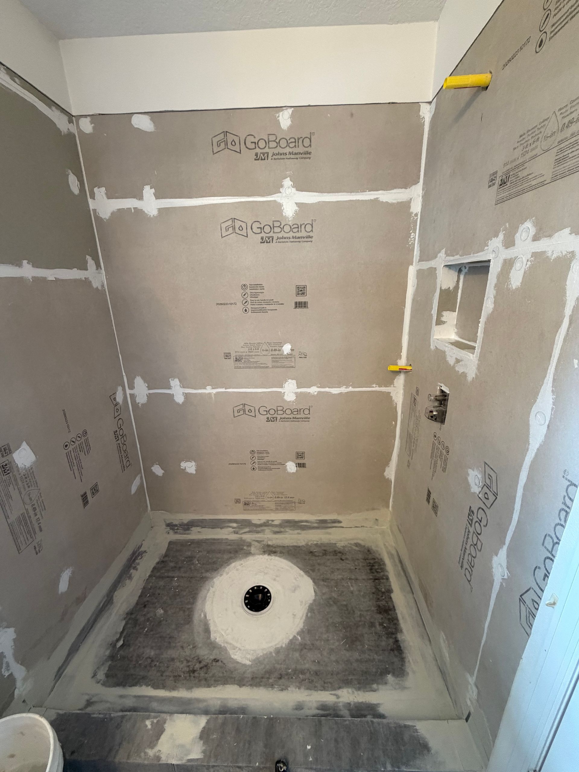 Partially tiled shower stall under construction with gray cement board and a floor drain.