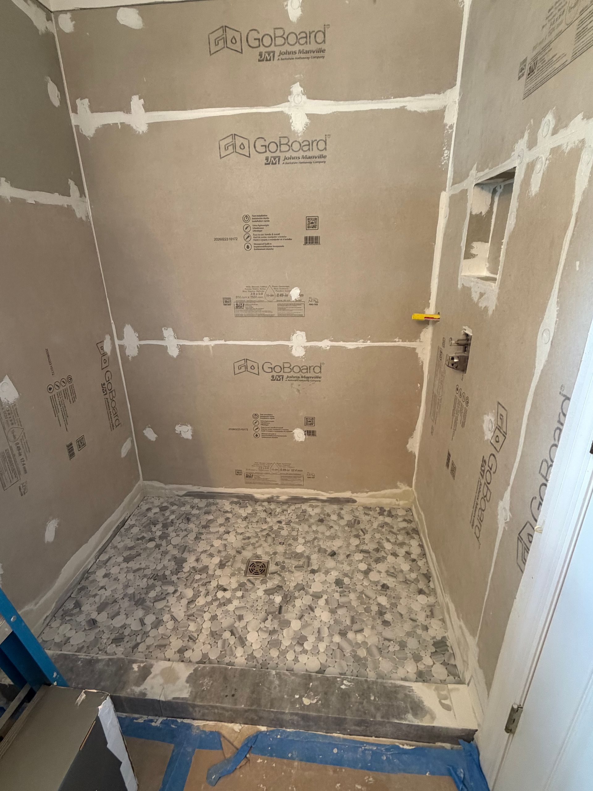 Small tiled shower under renovation with unfinished drywall and a blue floor protector.