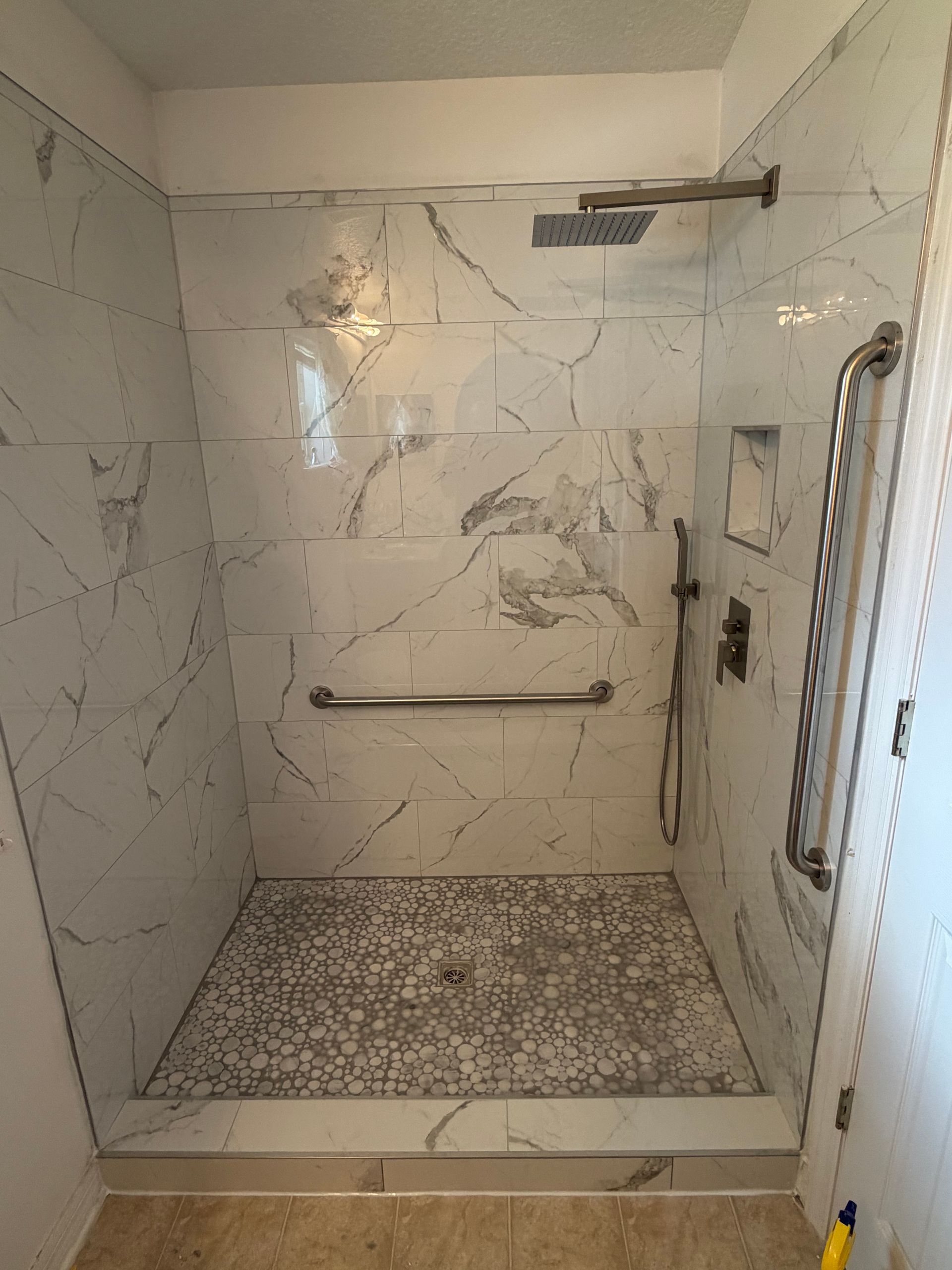 White tiled walk-in shower with built-in bench, grab bar, handheld shower, and low-threshold entry.