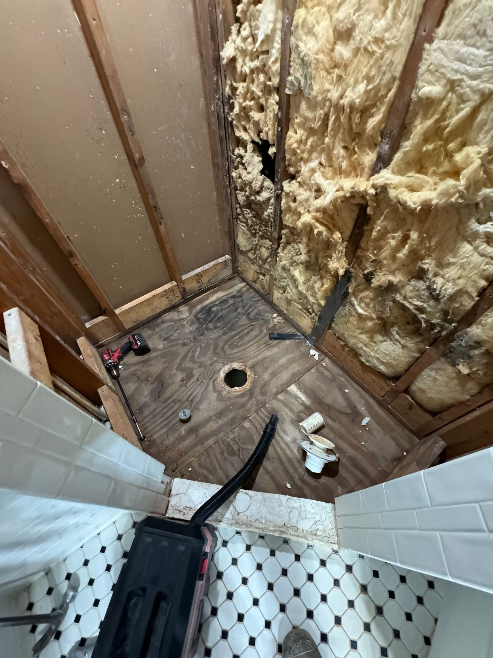 Partially renovated bathroom with exposed insulation, tiled shower floor, and a drain hole