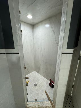 Small white tiled shower stall with recessed lights, a red bottle, and a tile scraper on the floor.
