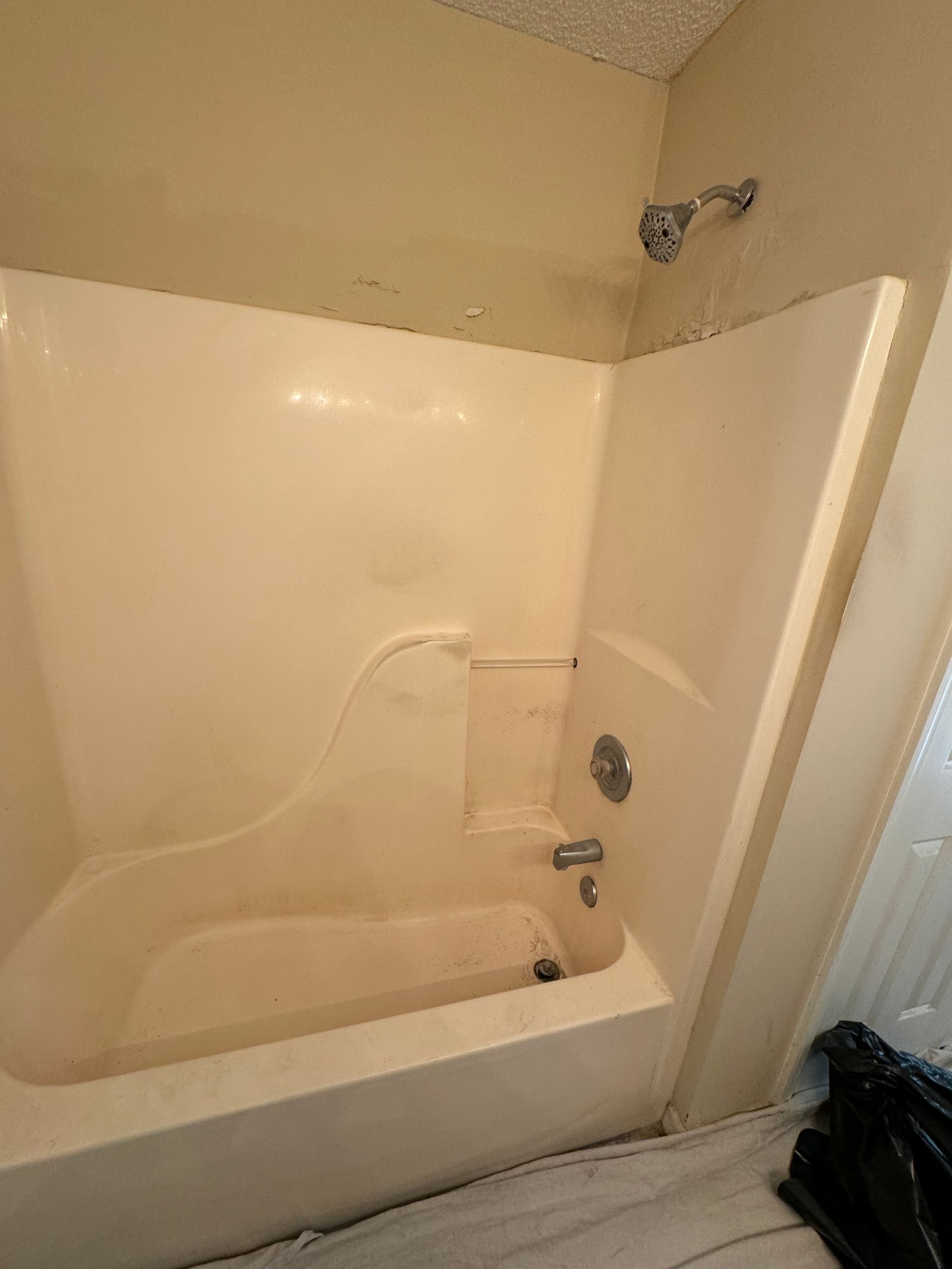 Empty bathtub and shower in a beige bathroom with a handheld shower head and curtain rod.