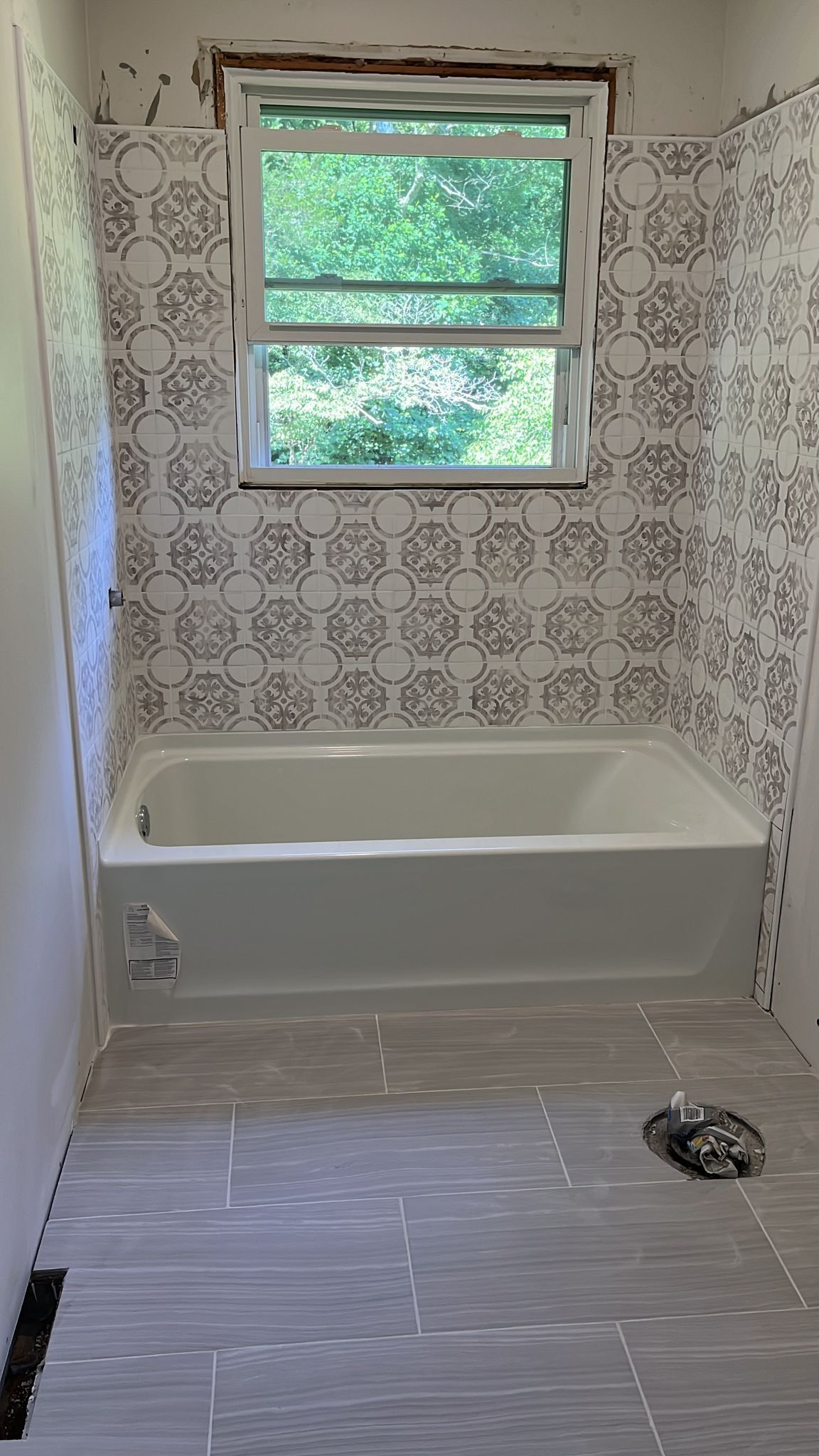 Small bathroom with tiled walls, window, bathtub, and exposed floor drain, mid-renovation.