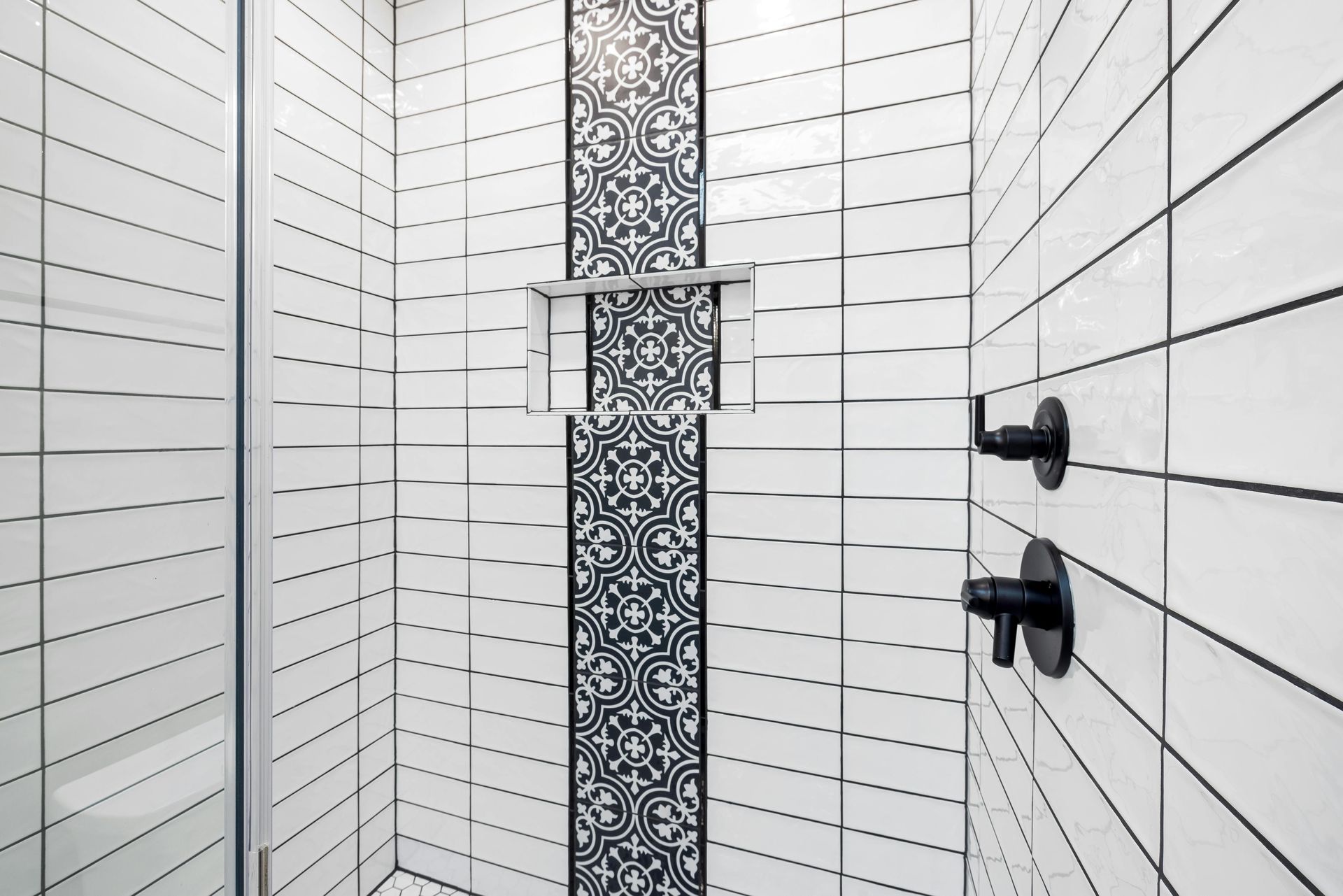Modern white-tiled shower with black fixtures and a mosaic accent strip