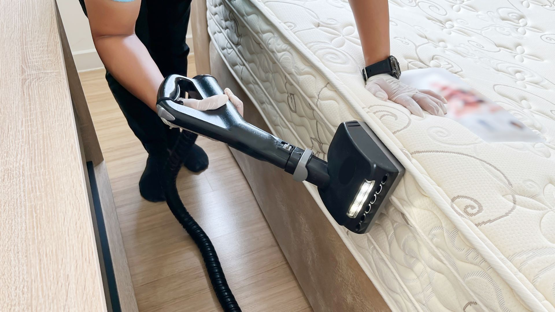 Person vacuuming a mattress with a handheld device in a bedroom.