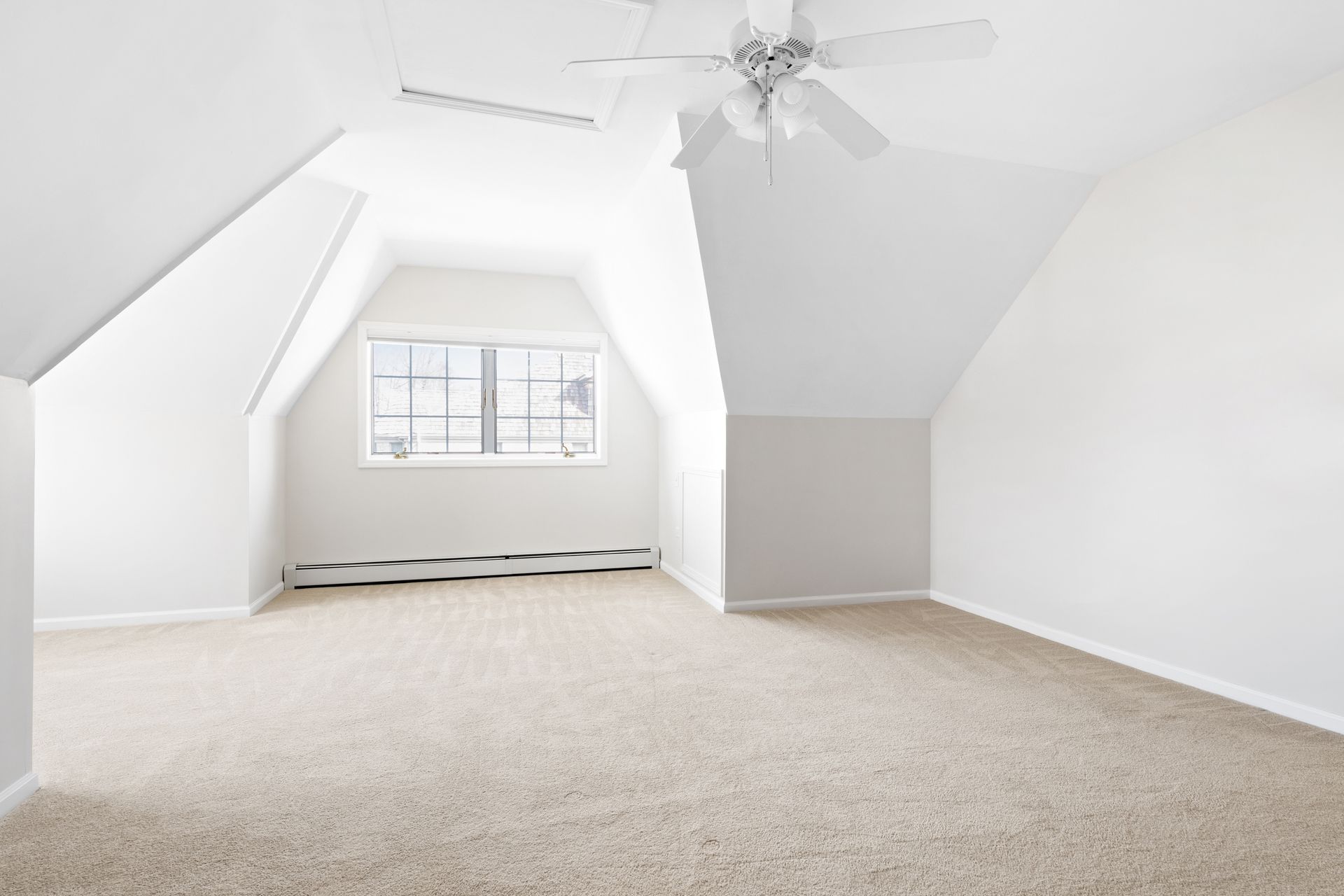 Empty attic room with angled ceilings, window, beige carpet, and ceiling fan.