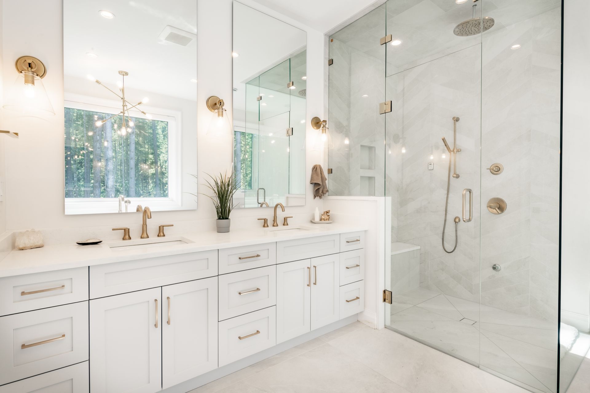 White bathroom with marble shower, double vanity, gold fixtures, and large mirrors.