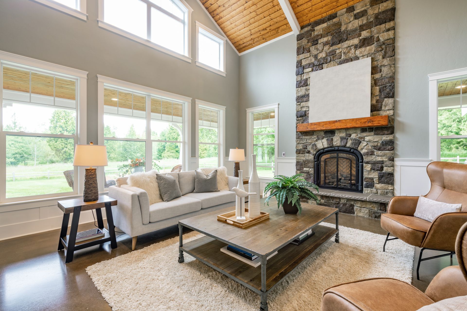 Living room with stone fireplace, large windows, white couch, and brown leather chairs.