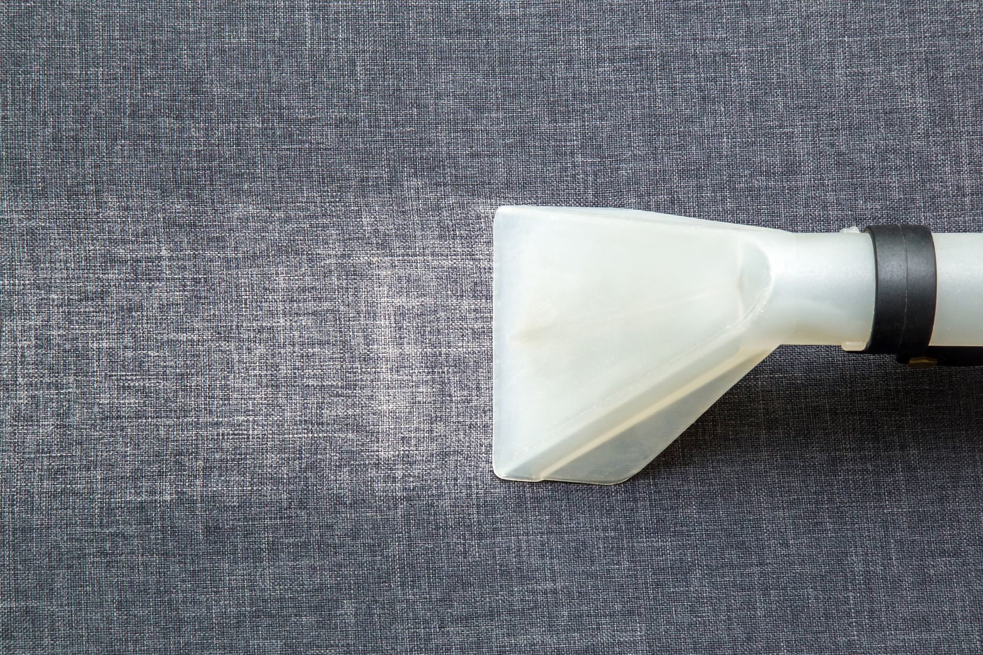 A white upholstery cleaner nozzle on grey fabric.