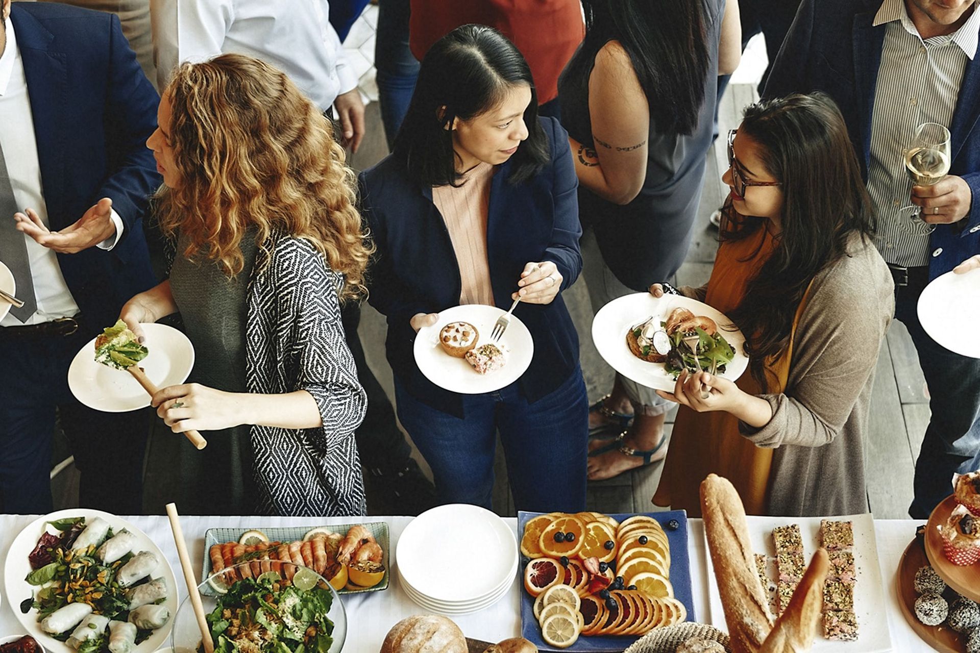 People at a buffet, selecting food. Salad, rolls, and appetizers are on the table.