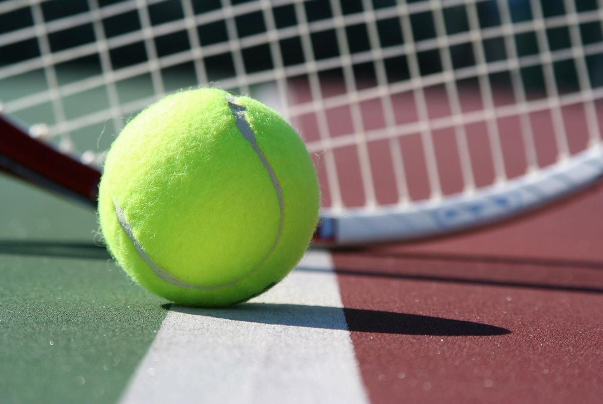Tennis ball on court with racquet behind it.