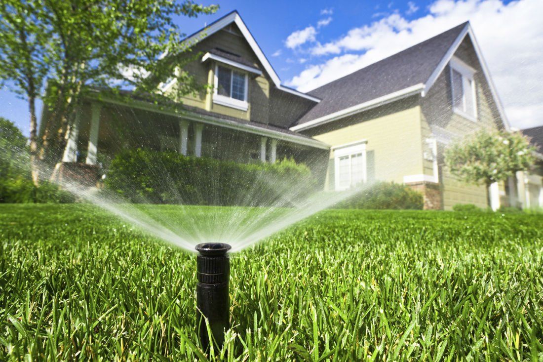 A lawn sprinkler is spraying water on a lush green lawn in front of a house.