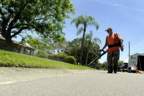 A man is blowing grass on the side of the road