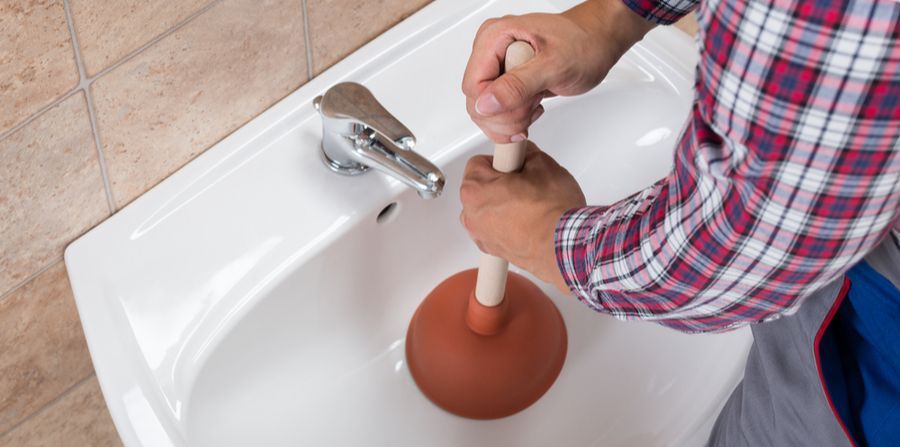 A man is using a plunger to unblock a sink.