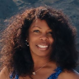 A woman with curly hair is wearing a blue dress and smiling.