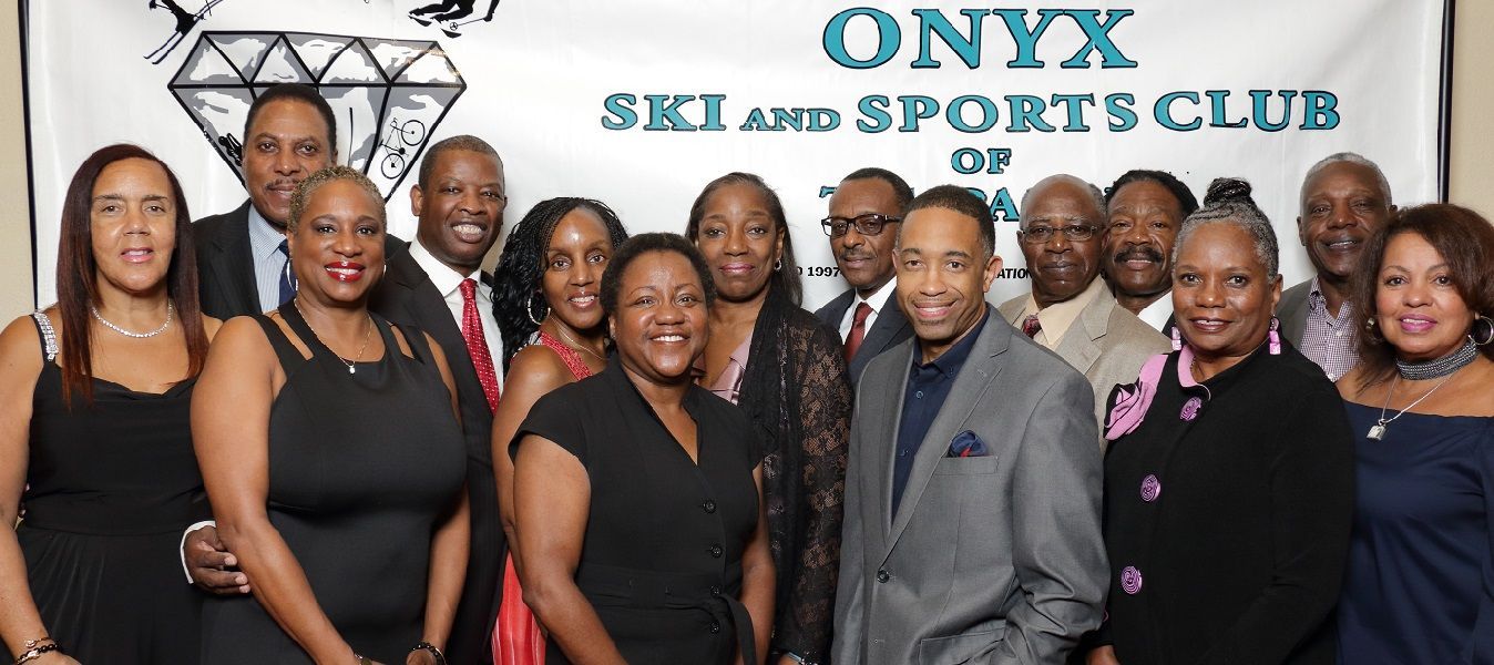 A group of people are posing for a picture in front of a banner that says onyx ski and sports club.