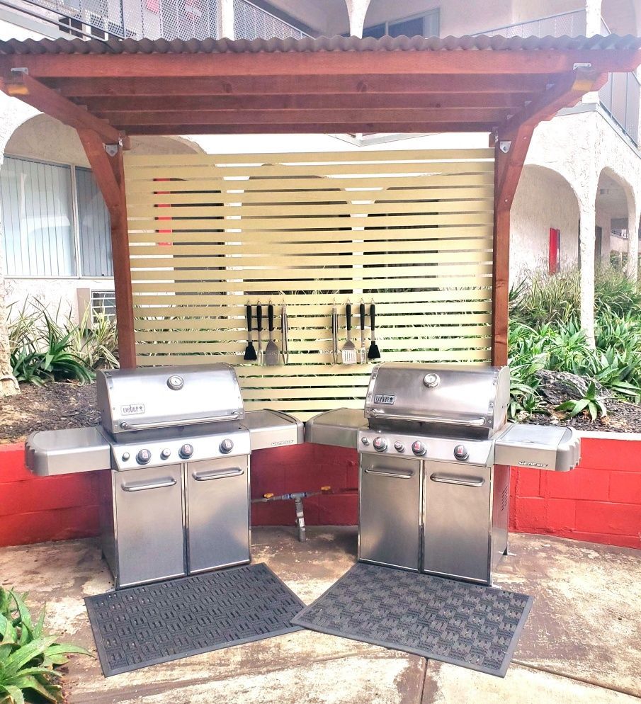 Two stainless steel grills are sitting under a wooden pergola.
