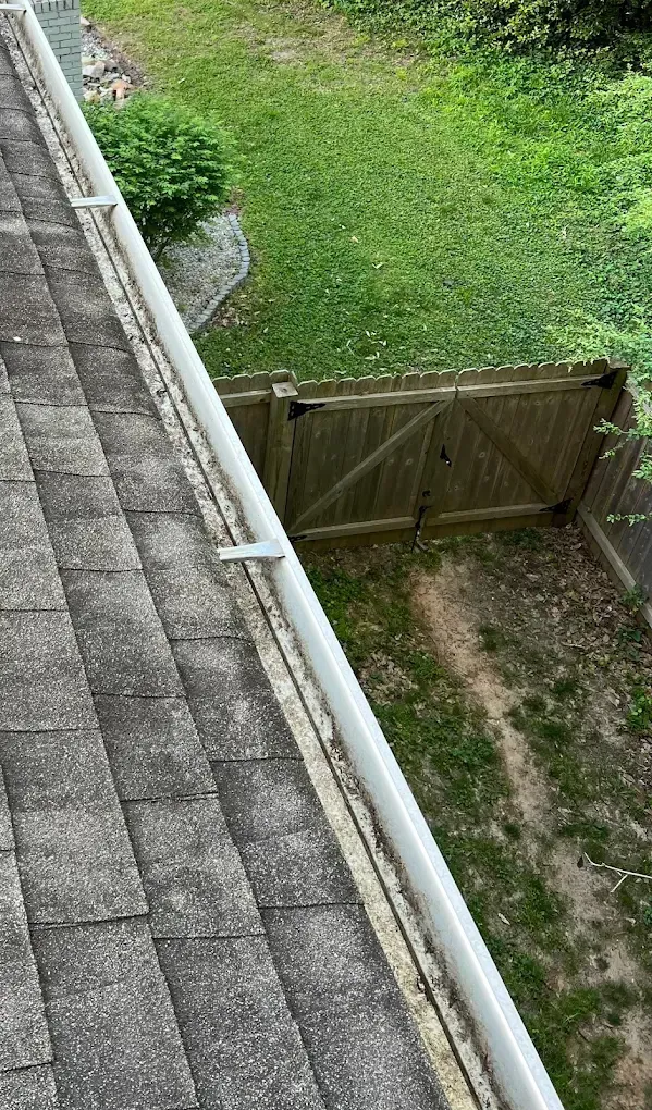 Roof with dirty shingles and filled gutter, fence, and grass.