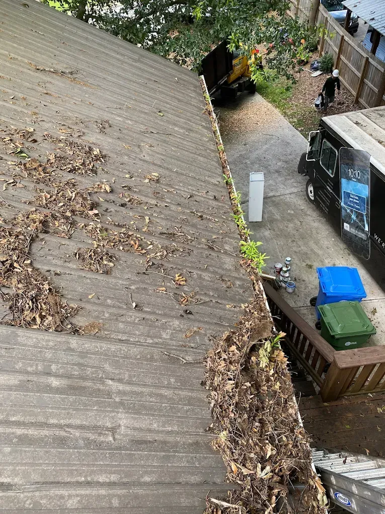 Roof with leaves, gutter clogged. A small vehicle is parked in the driveway.