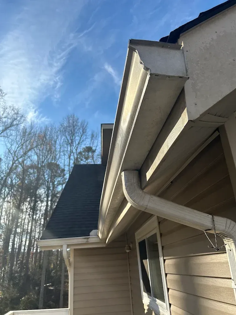 White gutter and siding on a house against a blue sky with visible trees.
