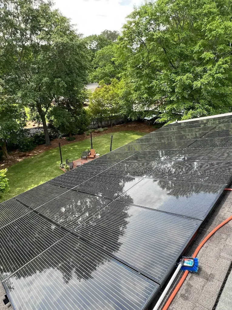 Solar panels on a rooftop, wet with water. Green trees and lawn in the background.