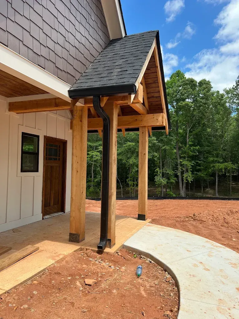 Entryway with a small roof, supported by wooden posts, with a black gutter.