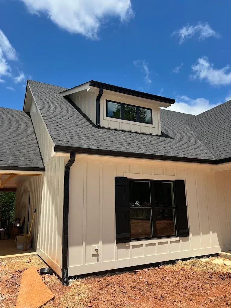 White house exterior with black trim, dark gray roof, and blue sky.