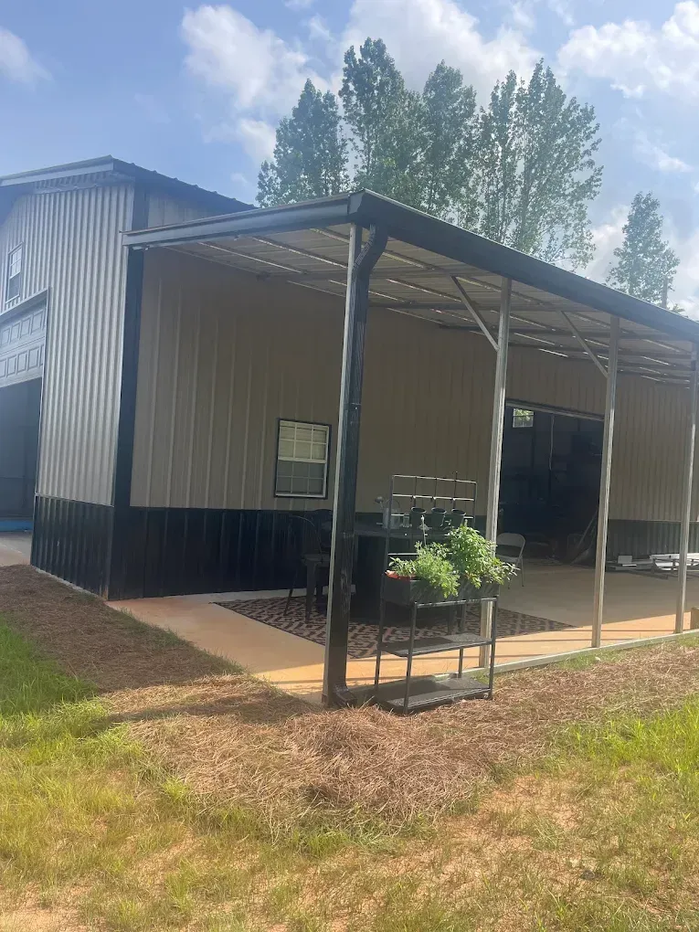 Metal building with a covered patio, featuring a dark base, light walls, and a small garden.