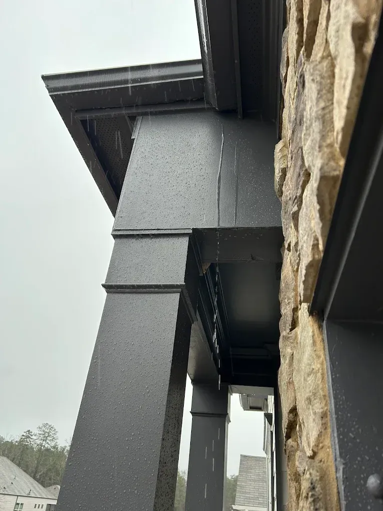 Exterior view of a dark gray porch with visible rain. Stone wall and part of a house roof are also present.