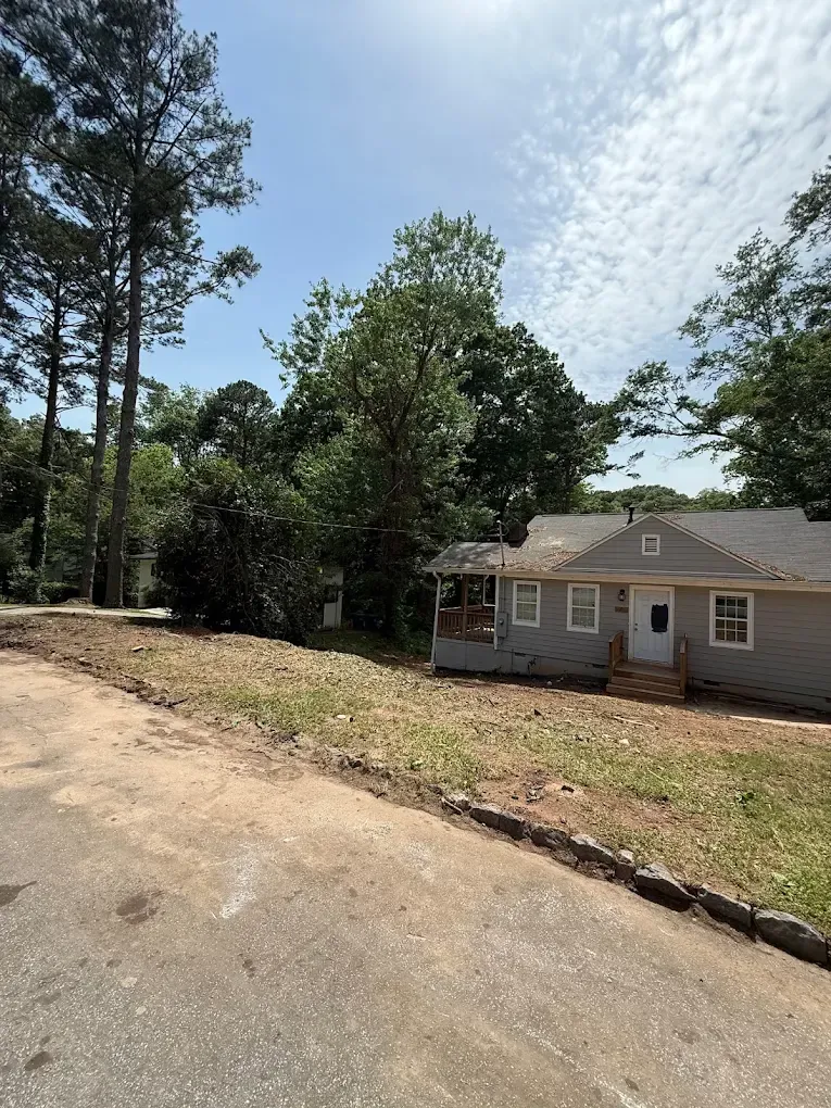 Gray house with porch, trees, and blue sky.
