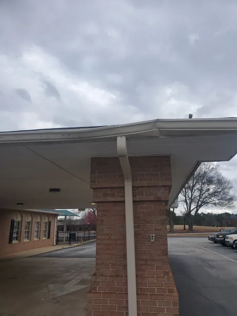 Brick pillar supporting a white roof with a gutter and downspout. Cloudy sky background.