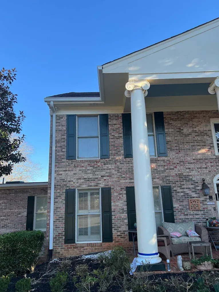 Brick home with white columns, green shutters, and blue sky.