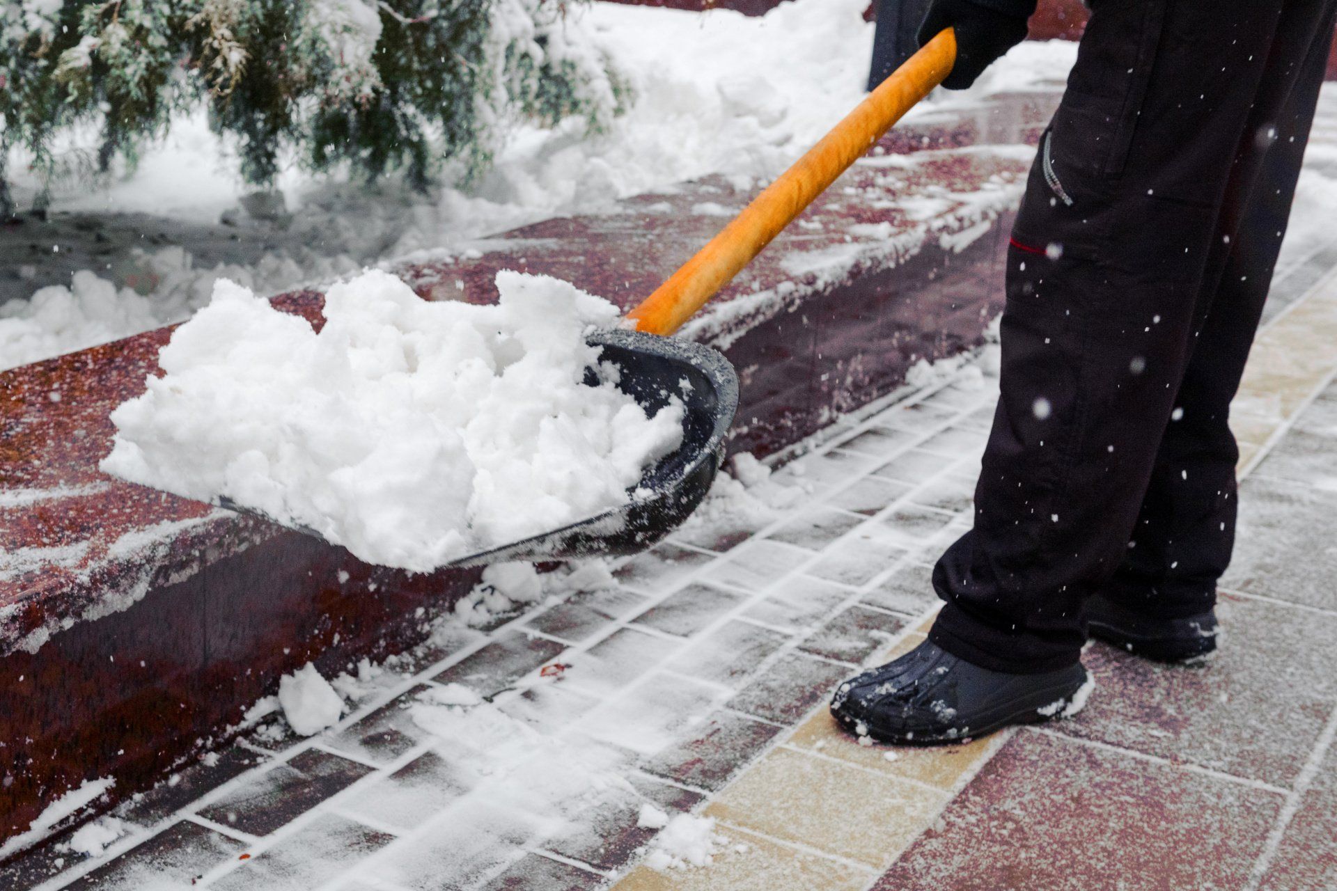 Eine Person schaufelt mit einer Schaufel Schnee vom Gehweg.