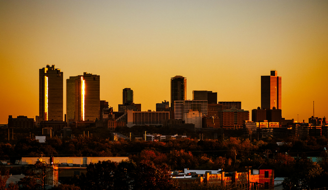 City skyline at sunset with tall buildings silhouetted against an orange sky