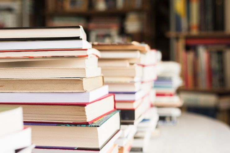 Stacks of books on a table, with a blurred bookshelf in the background.