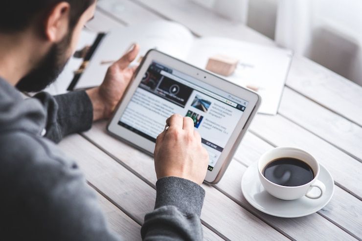 Man using tablet, reading news, with coffee on a white table.