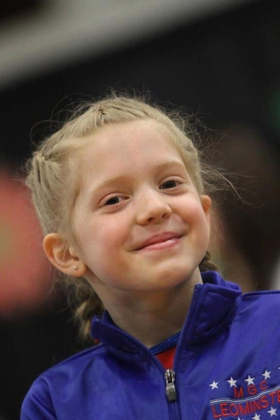 Young girl with blonde hair in braids, smiling, wearing a blue jacket with 