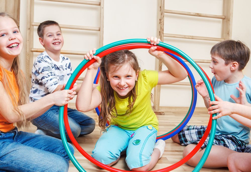 Four children playing with hula hoops indoors, smiling.