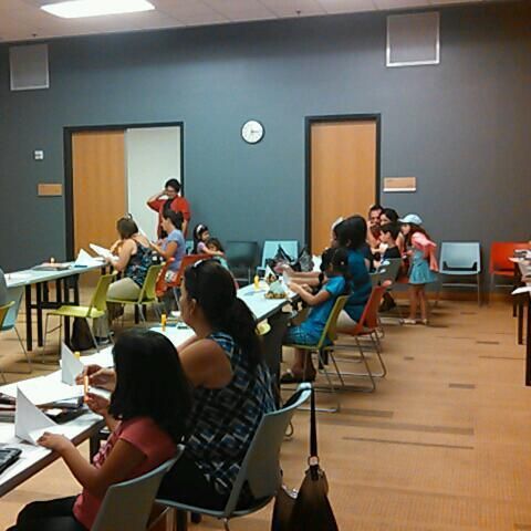 People seated at tables, crafting in a room with a clock on the wall and chairs.