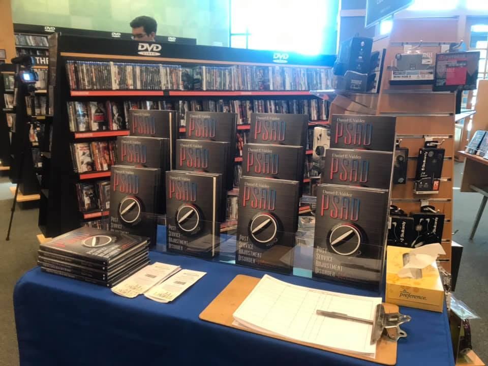 Books on display in a store, stacked on a blue table. A person is visible in the background.